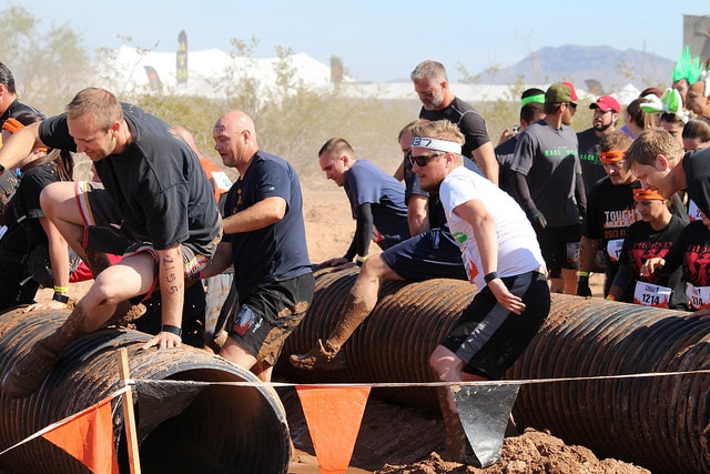 Sport men participating in obstacle race competition over jumping tubes.