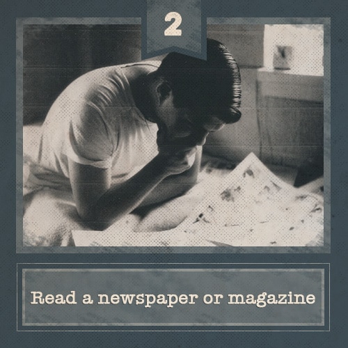 Man sitting on bed and reading newspaper.