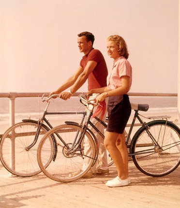 A man and woman, dressed in summer attire, standing on a boardwalk with bicycles.