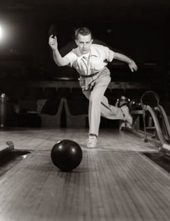 In this black and white photo, a man bowls a ball with precision and skill, aiming for a strike.