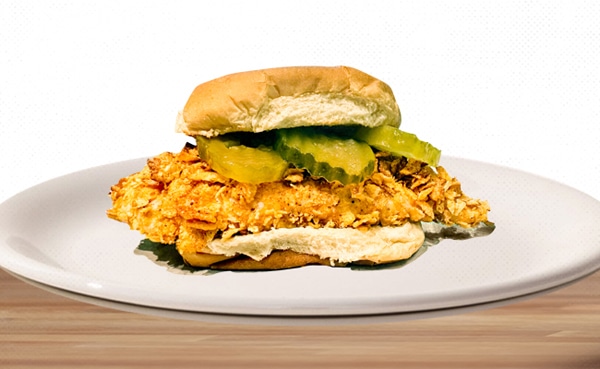 Healthy crispy chicken sandwich with pickles on a white plate.