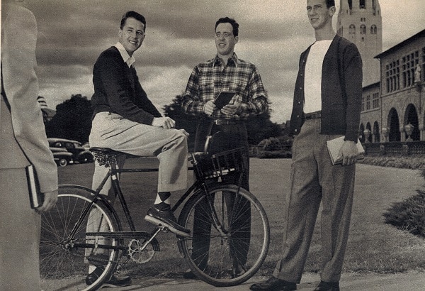 A group of students standing around the professor at bicycle. 