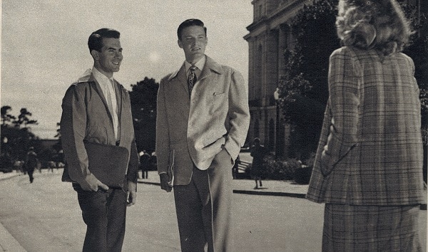 A woman walking toward men standing in suit.