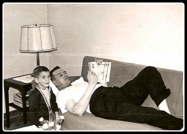 Father Lying on Sofa reading book with child.