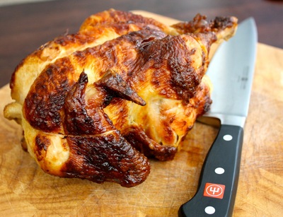 A delicious store-bought rotisserie chicken on a cutting board with a knife.