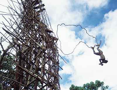 A man is performing an insane jump from a tall wooden structure, undertaking a male rite of passage.