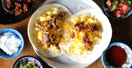A plate of breakfast tacos and salsa on a wooden table.