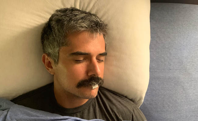 A man with a mustache sleeping in bed at night.