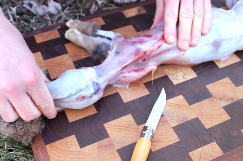 Man cutting off the rabbit meat with knife.