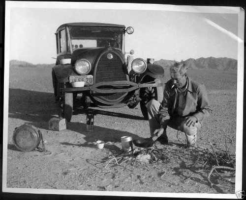 A man taking an impulse road trip, kneeling next to a car in the desert.