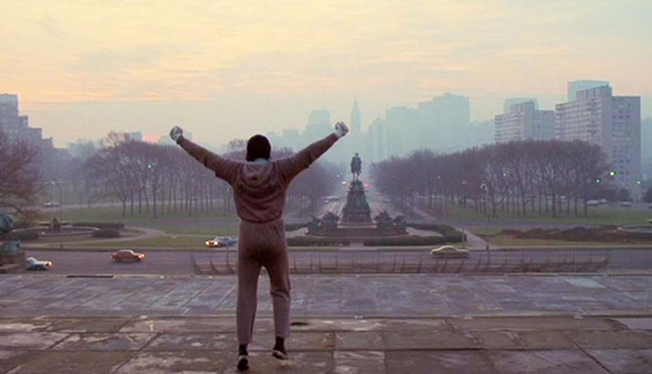 A man with his arms raised in the air in front of a city after completing his training.