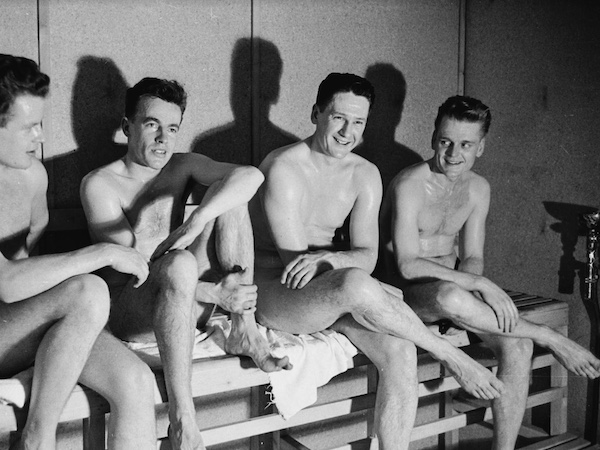 A group of naked men observing sauna etiquette while sitting on a bench.