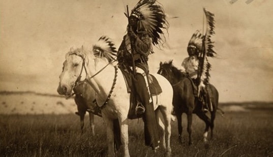 A black and white photo of a group of Sioux men on horses displaying physical toughness.