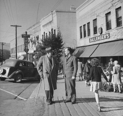 Two men, one of them holding a child, standing on a street corner and discussing the urgency to take action now.