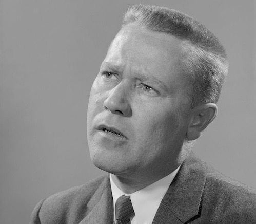 A black and white portrait of a man in a suit and tie with a contemplative expression, looking slightly upwards, radiates an aura of metacognition.