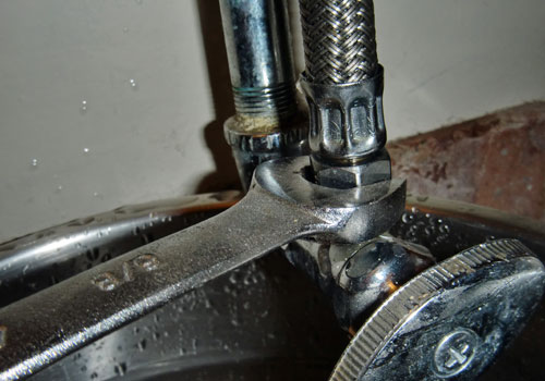 Loosening toilet supply hose valve with wrench close up.