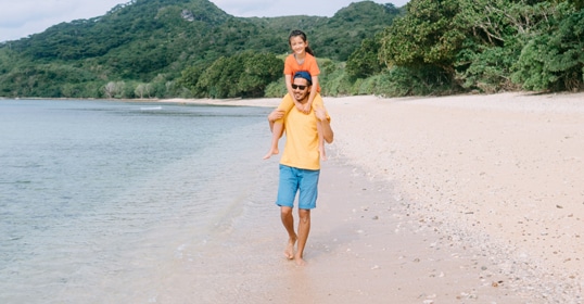 Father shedding pounds while carrying his child on his shoulders, walking along a beach.