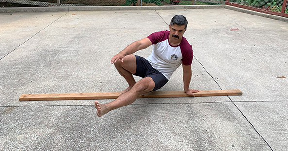 A man balancing on a 2x4 in a parking lot.