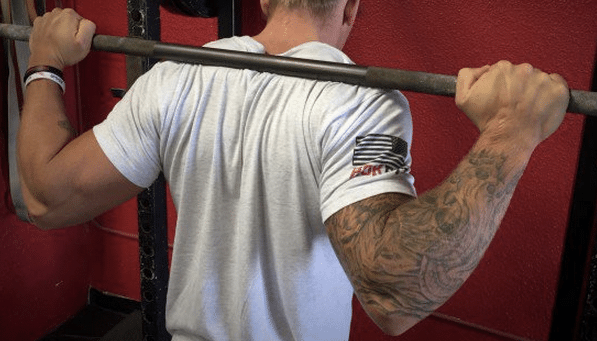 A man with tattoos is seen pumping iron in a gym.