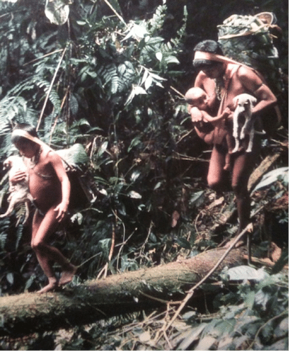 Vintage women carrying children and dog while crossing tree trunk. 