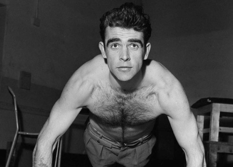 A shirtless man breaking through a plateau in a gym while doing push-ups.